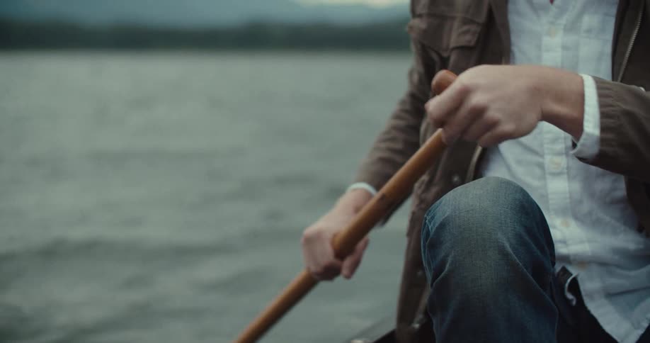 A person is rowing a boat with a wooden paddle on a lake
