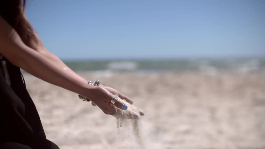 A woman picks up hands full of sand on a beach
