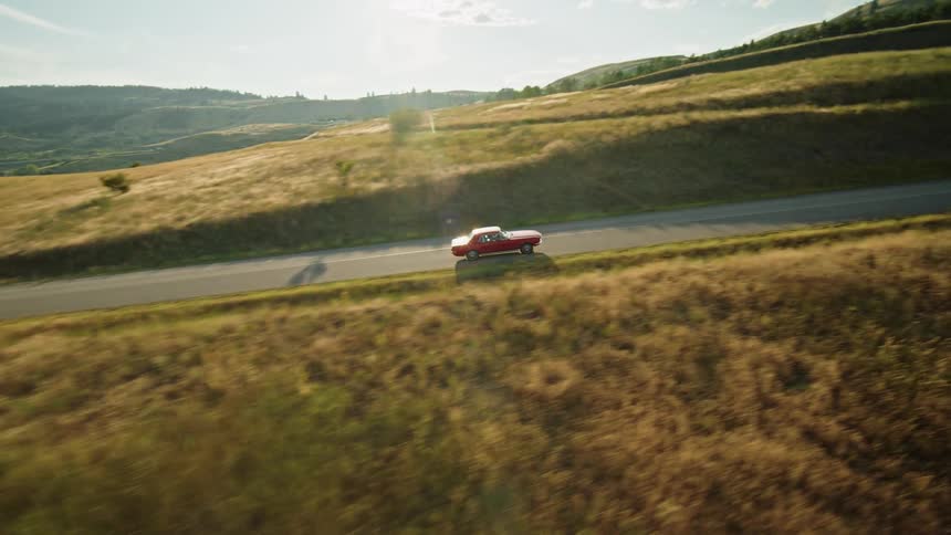 A car drives down a road that runs through rolling hills