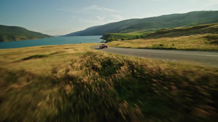 A red car driving on a lonely road in a rural area flanked by grasslands on both sides at midday