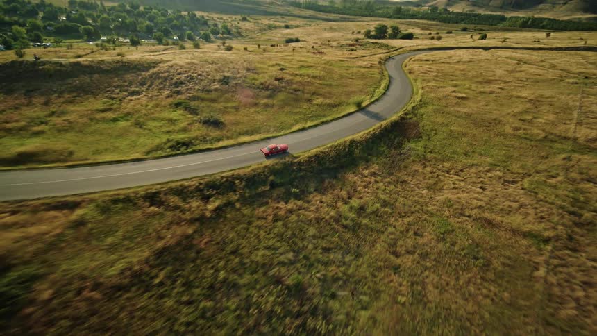 A car drives on a winding countryside road beside a lake