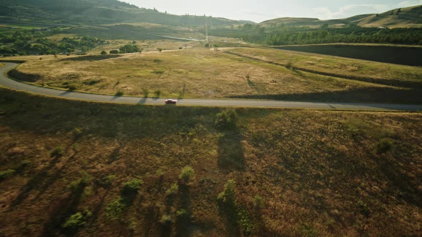 A red car drives on a winding road through the countryside