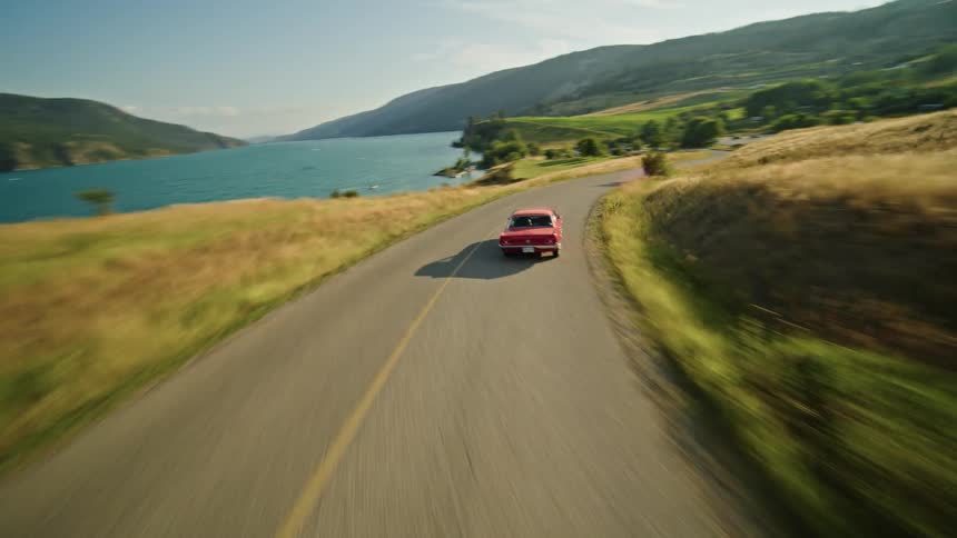 A car drives along a road that curves through a landscape of fields and hills
