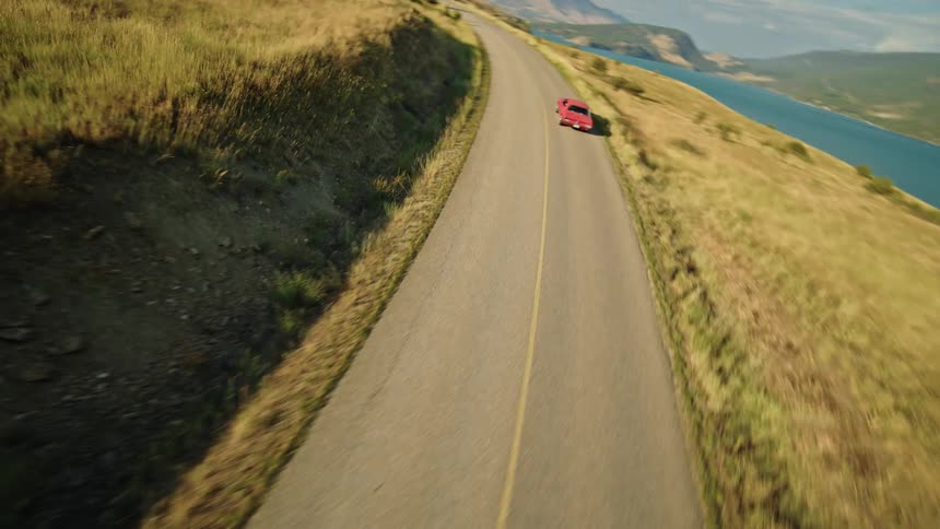 A drone follows a car as it drives on a road through hills on the coastline