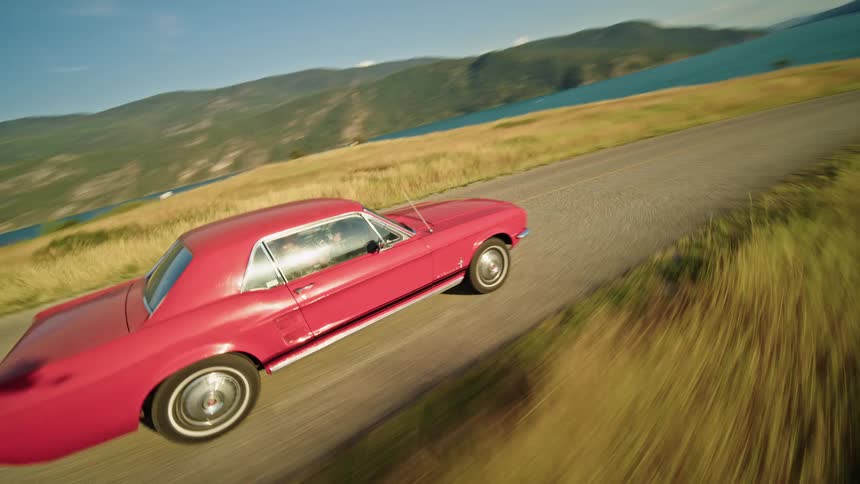 Classic red car traveling along a road through the mountains and along the seashore