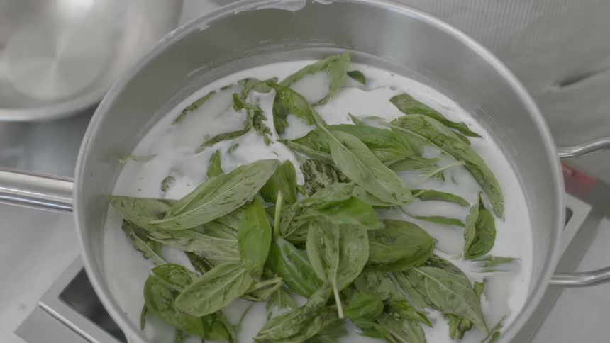 A person adds fresh herbs to a pot of ingredients