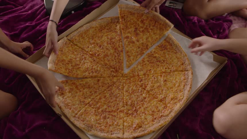 Friends sit together grabbing slices from a giant cheese pizza