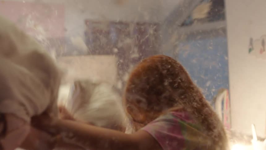 Girls laugh together during a playful pillow fight indoors
