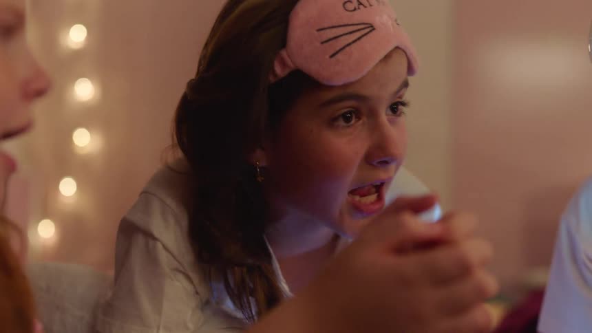 Teenage girls having a sleepover lying on the bed and telling scary stories at night
