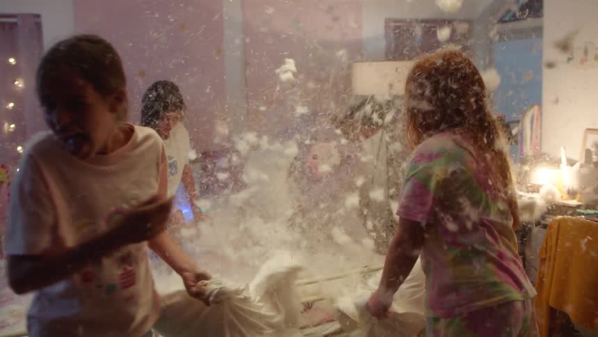 Children have a playful pillow fight in a bedroom