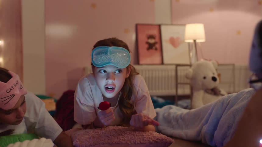 Kids have a sleepover in the bedroom as a girl tells a flashlight story
