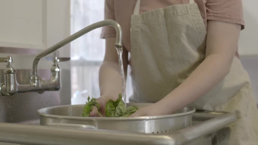 A woman washing a large pot of vegetables