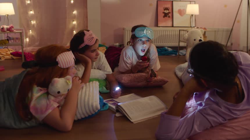 Four kids at a sleepover lie on the floor telling a spooky story