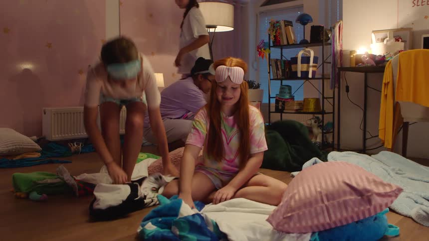 A group of four teenage girls setting up blankets on the floor having a sleepover in their pajamas