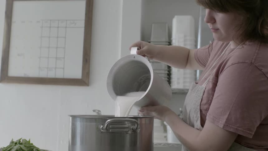 A woman adds milk to a large cooking pot