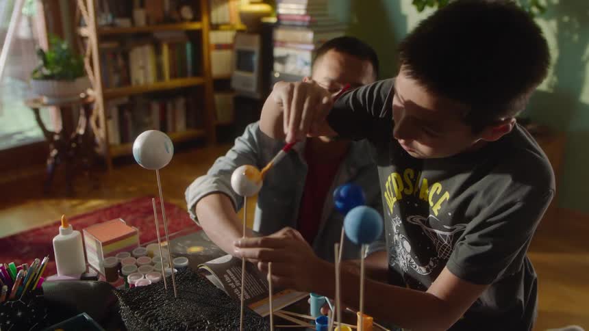 A father and son work on a solar system painting project together