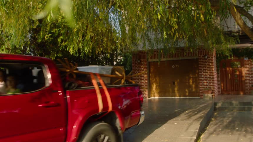 A red truck sits in a driveway in front of a house as a man ignites the car and go to the street