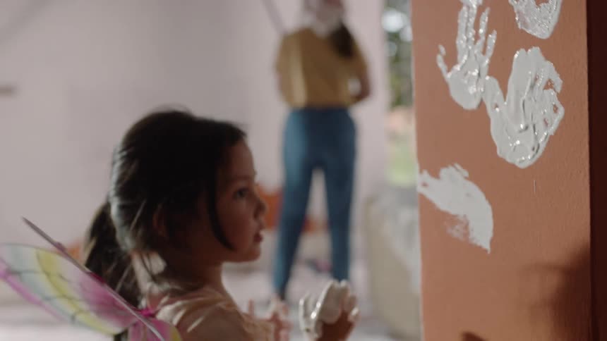 Girl with costume wings paints the wall leaving white handprints