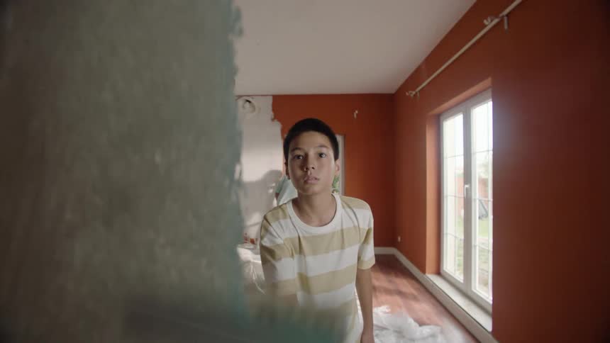 A family of threea man a woman and a teenage boypainting the living room wall at midday