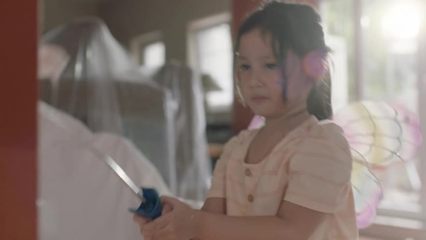 Little girl in fairy dress painting the wall with white paint