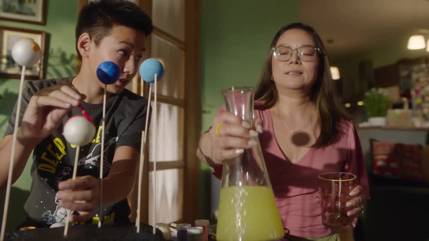 A mother and son work together on painting a solar system model at a table
