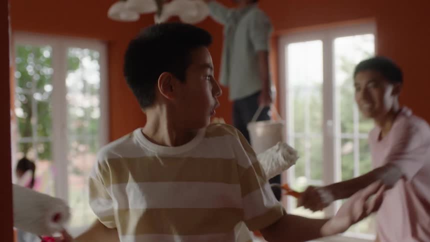 Family painting the walls of their house while one boy plays with the other with paint rollers