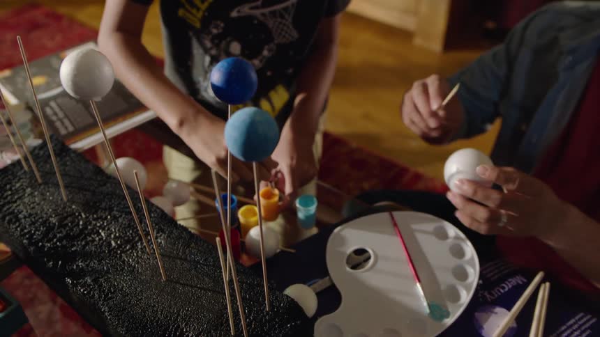 A man and a boy sit at a table and work on a solar system model
