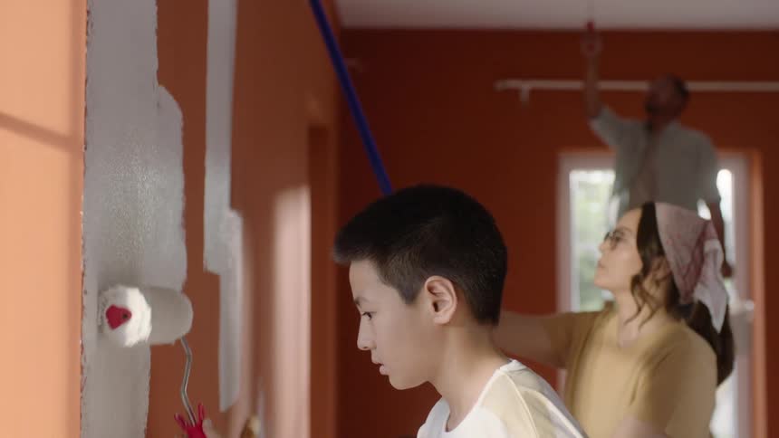 Boy and woman paint the orange walls white with paint rollers