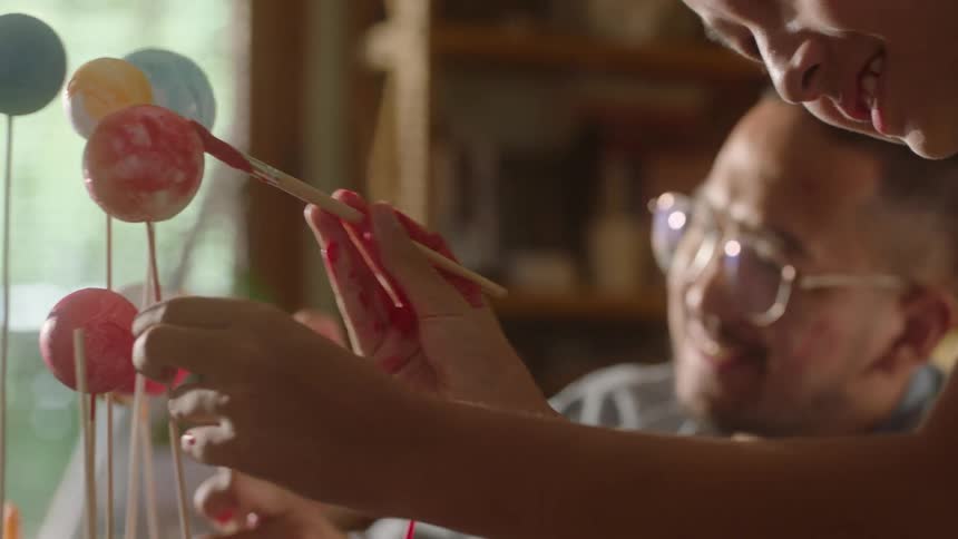 A father and son paint small balls on sticks