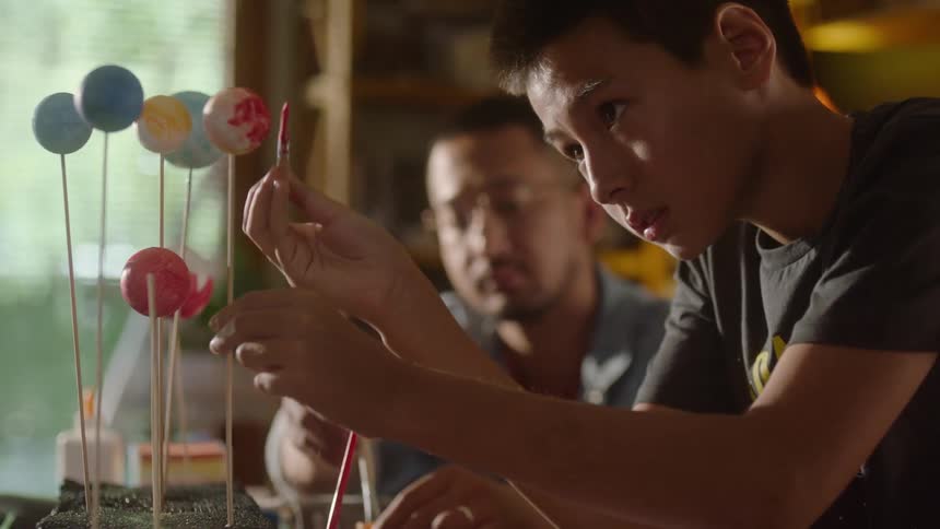 Father and son paint a solar system model together at a table