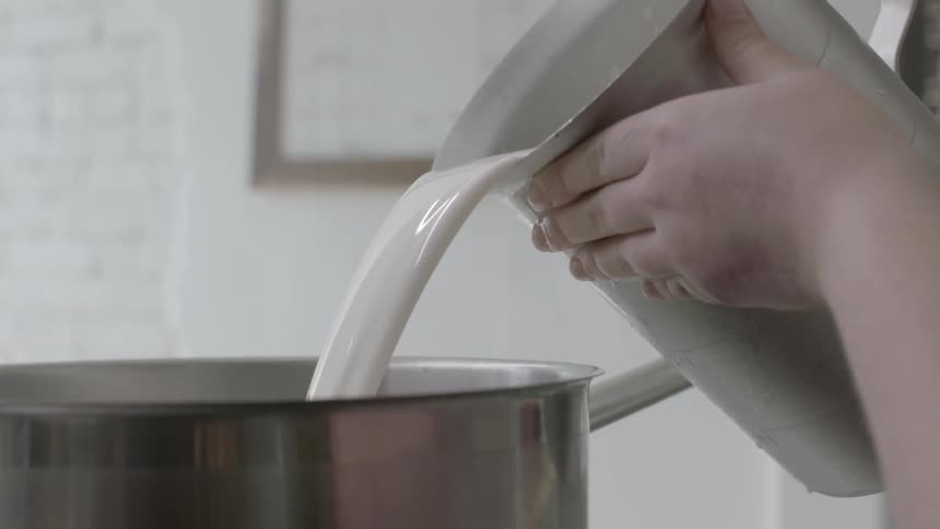 A woman pours a mixture into a vat