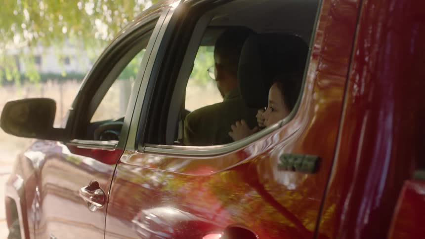 Child looks out the window of a red pickup truck while an adult gets in