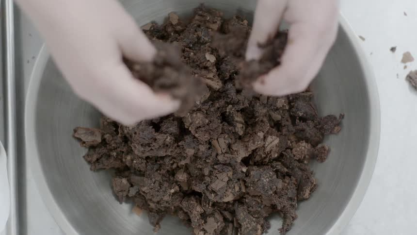 A woman breaks up chocolate in a bowl