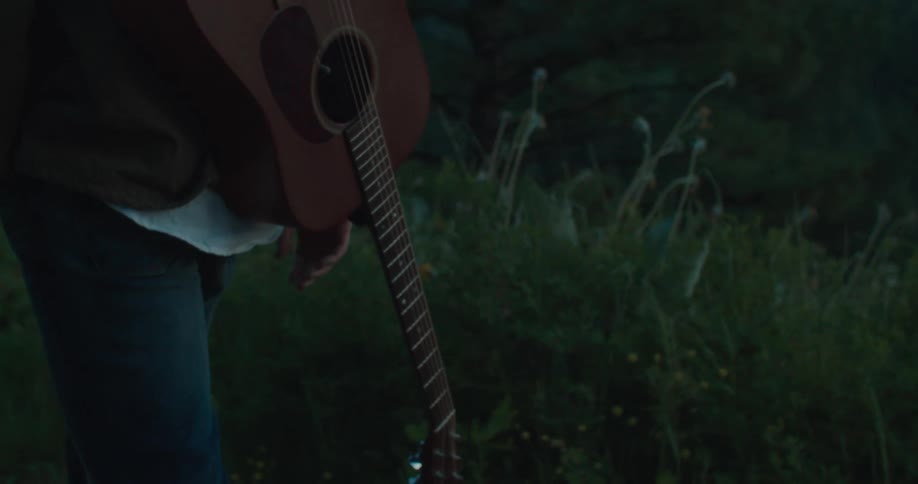 Person walking outdoors in the late afternoon with a guitar