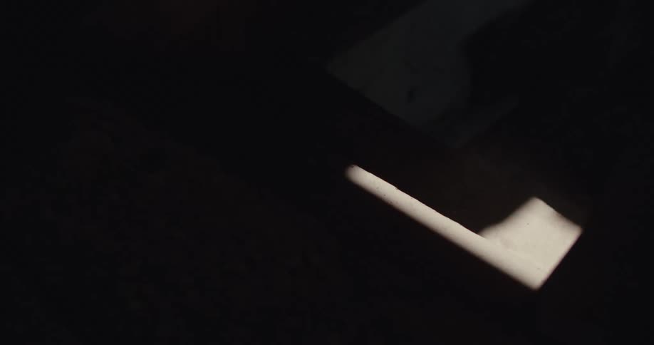 A single shaft of light illuminates a dark nondescript surface within what appears to be an interior space