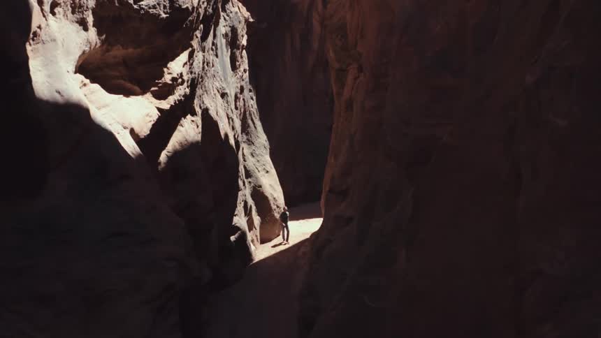A lone person stands illuminated within a deep shadowed canyon