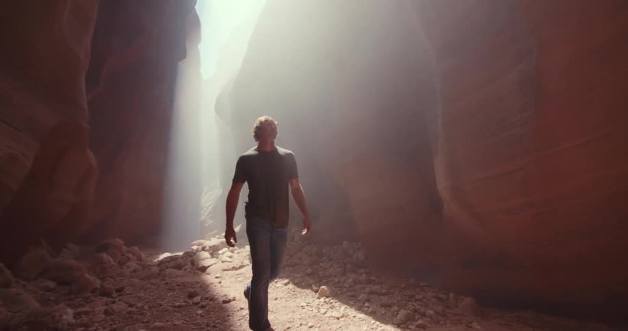 Man walking along a trail between reddish rocks