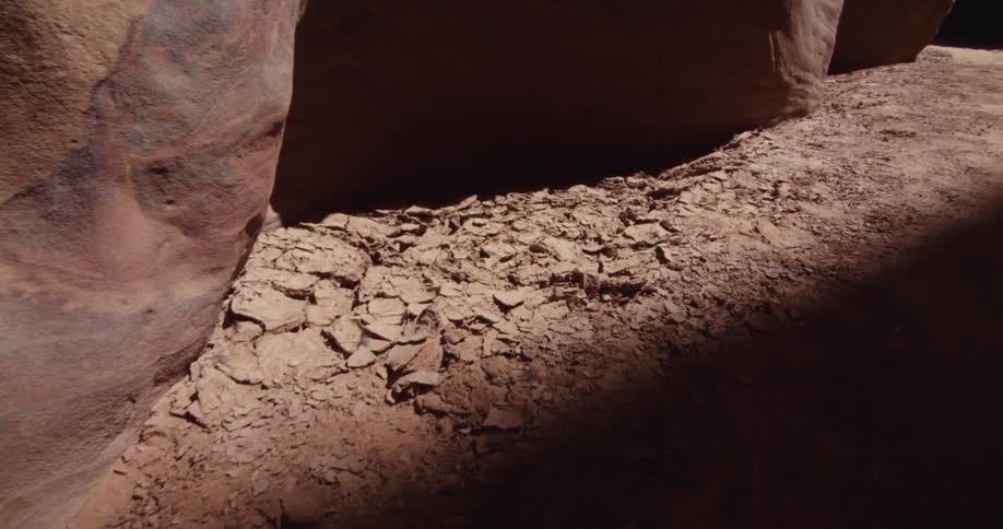Sunlight streams into a canyon illuminating cracked earth composed of many small dry irregular pieces