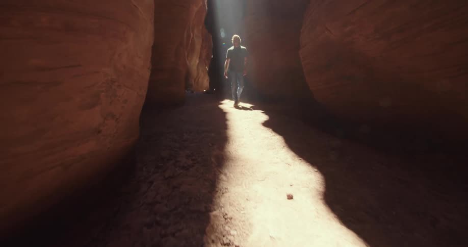 A lone figure walks through a sunlit slot canyon