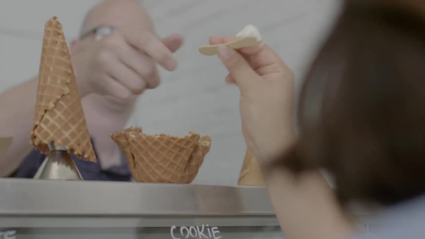 A man hands a woman a sample of ice cream