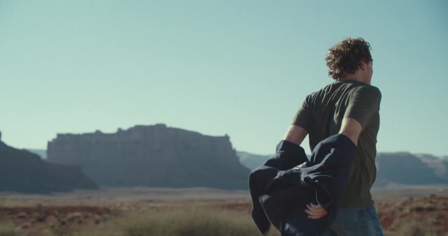 Man taking off his jacket and running in a natural environment with a canyon in the background