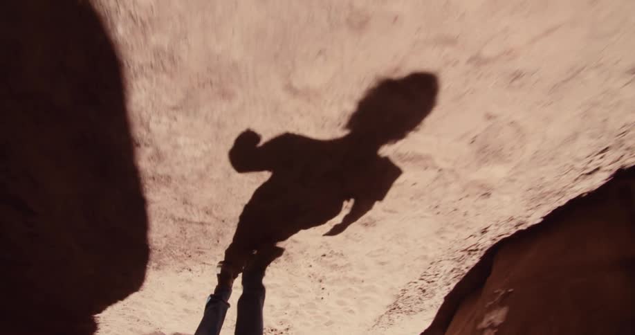 A persons shadow is cast on a rocky canyon floor in bright sunlight