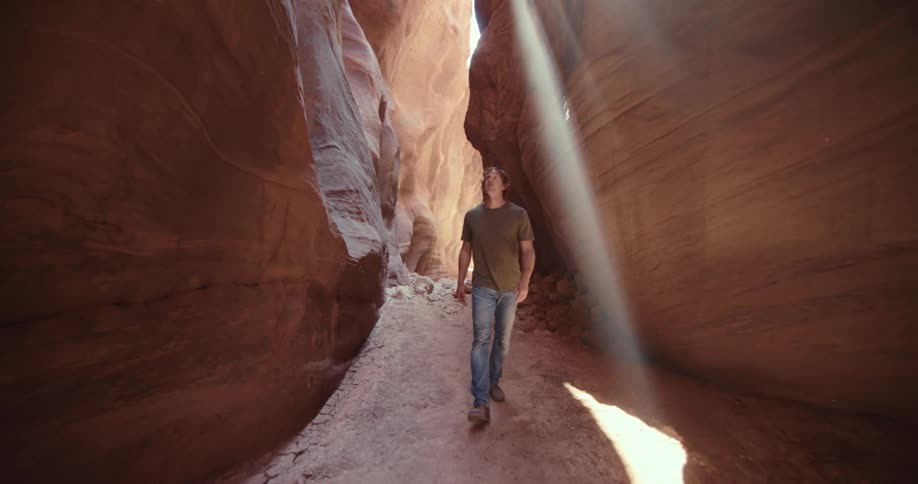 A man walks through a narrow canyon as sunlight streams down