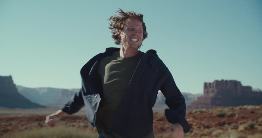 A young man excitedly running across a badland under the sun