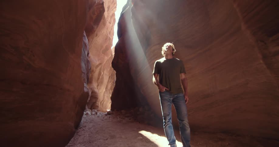 A male figure calmly walks through a sunlit slot canyon
