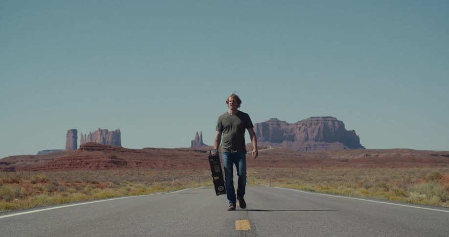 A man walking in the middle of a freeway holding a guitar on a sunny day