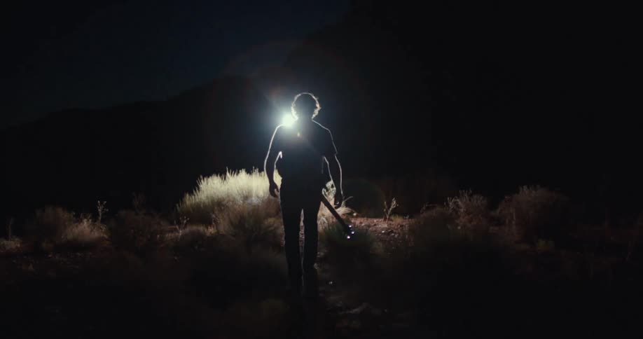 Man walking towards a light on a trail at night