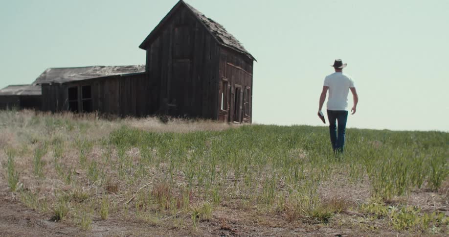 Man in hat and jeans walking towards barn