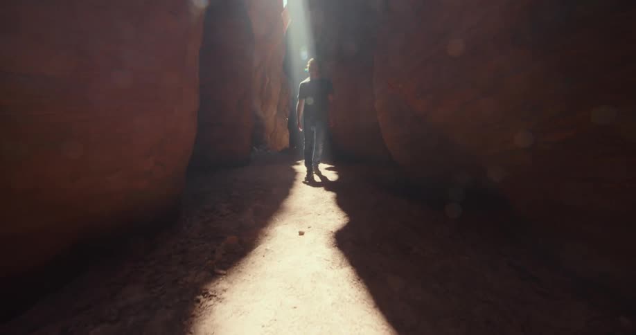 A man walks through a narrow canyon illuminated by a beam of sunlight