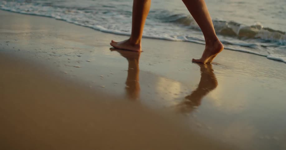 Female legs walking on the beach next to the sea outdoors during dusk or dawn